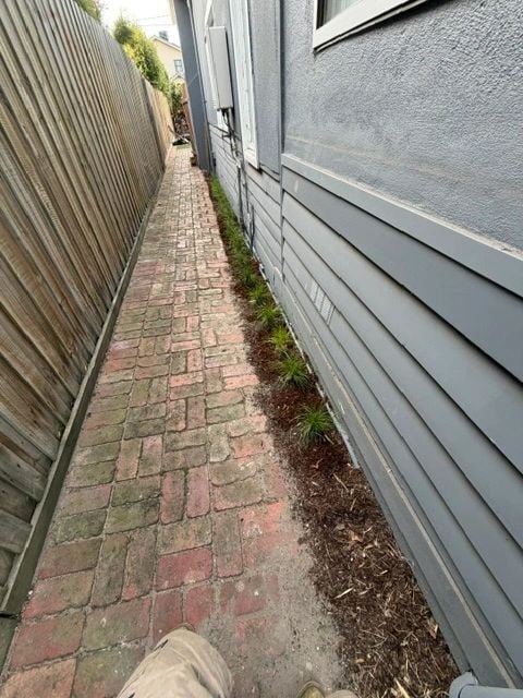 Narrow side garden bed freshly weeded and mulched along a brick path
