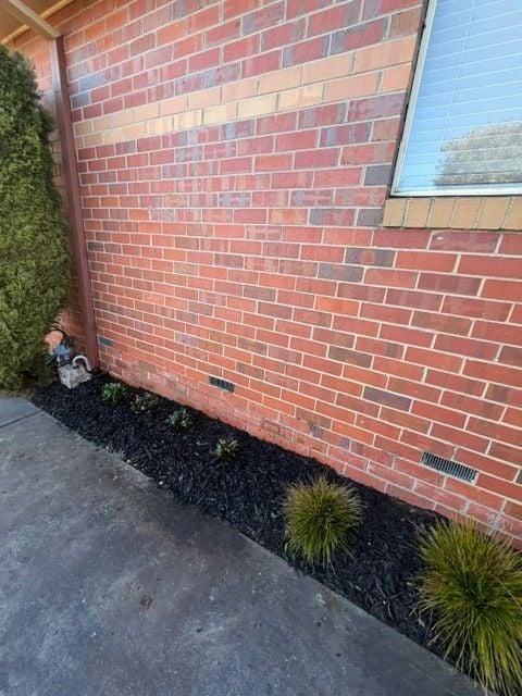 New garden bed with fresh mulch and grasses against a brick wall